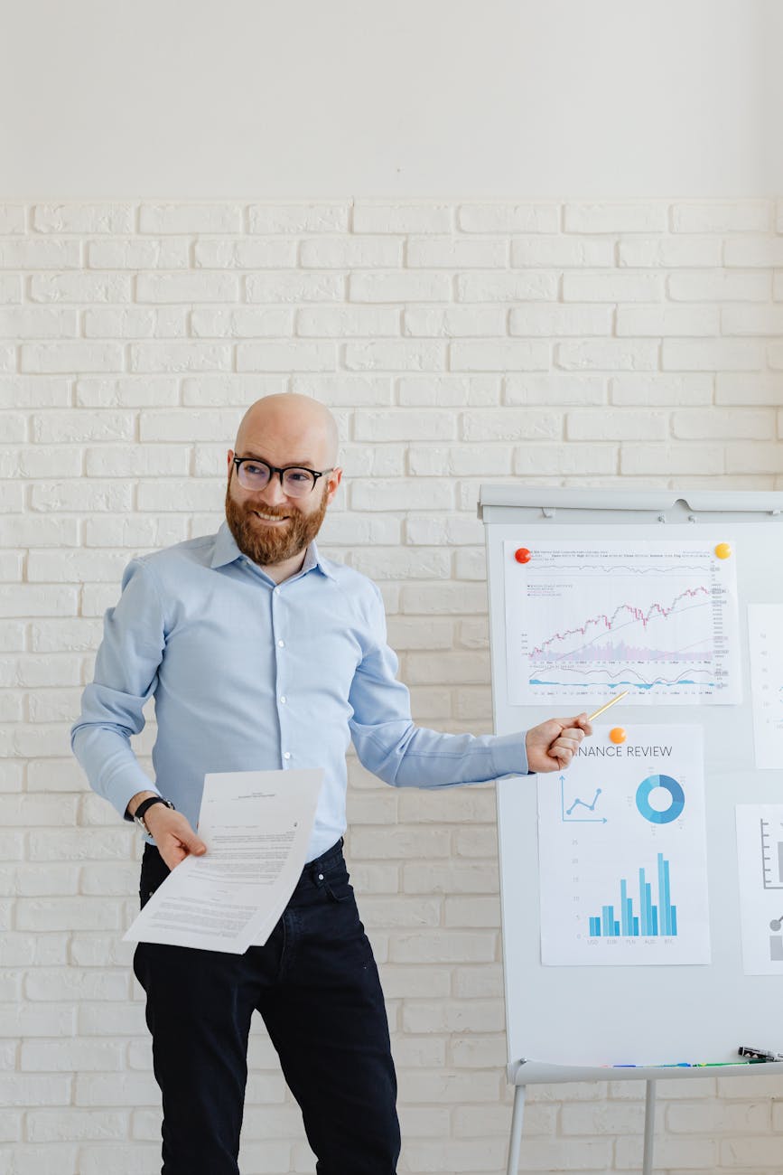 Smiling businessman with beard presenting financial charts at an office meeting.